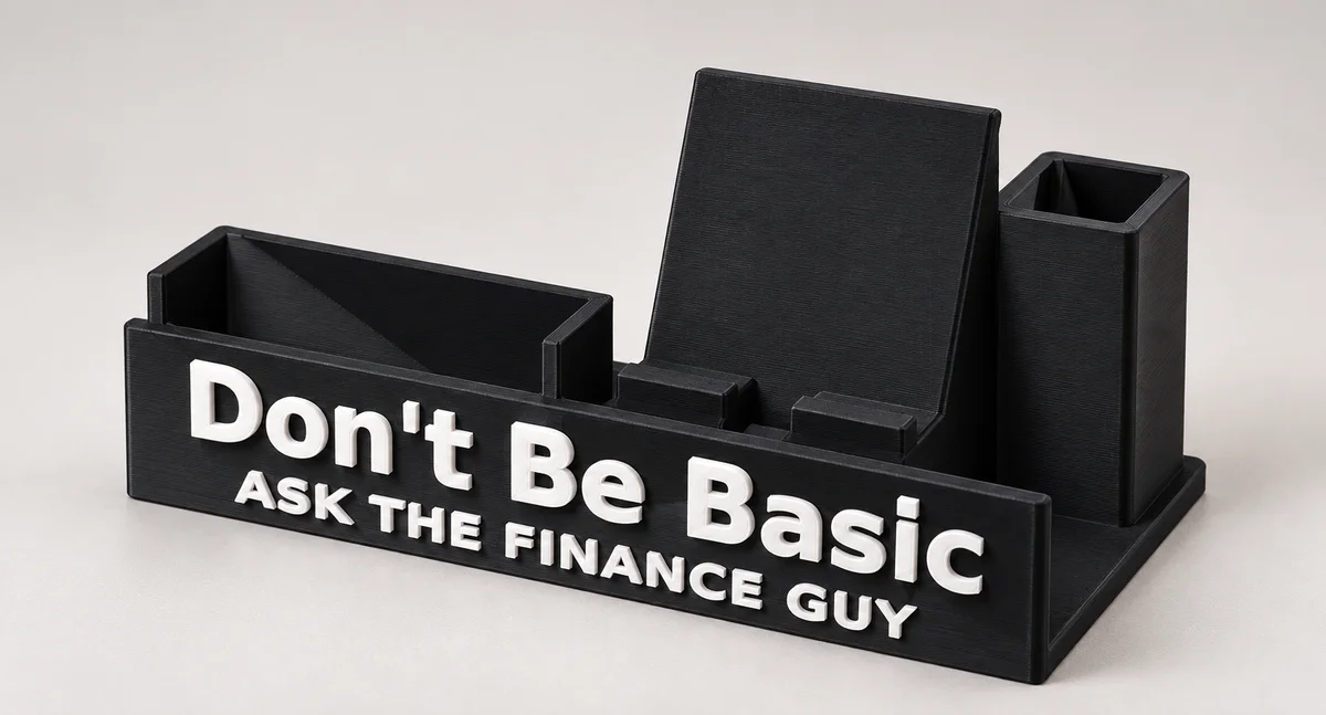 Completed black desk organizer: business-card pocket on the left, tilted phone stand in the middle, pen cup on the right, and individually attached white Don't Be Basic and Ask The Finance Guy lettering